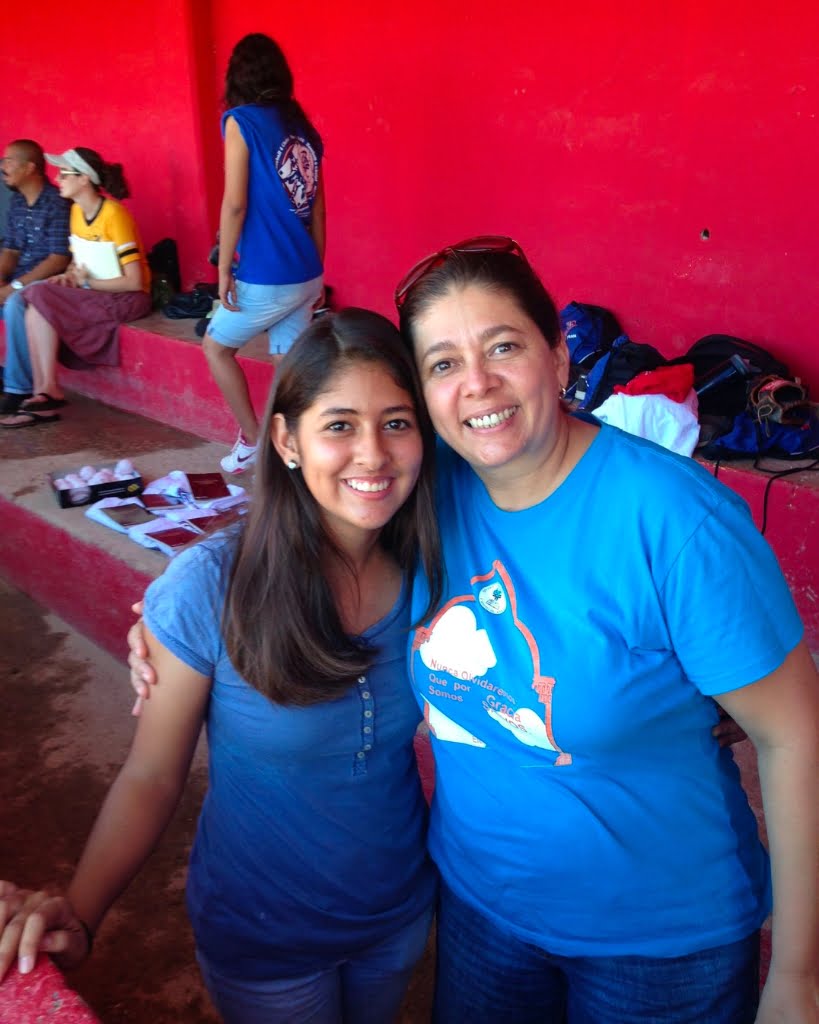 Two women posing for a photo at home in a baseball field.