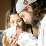 A man and woman are holding a newborn baby at home.