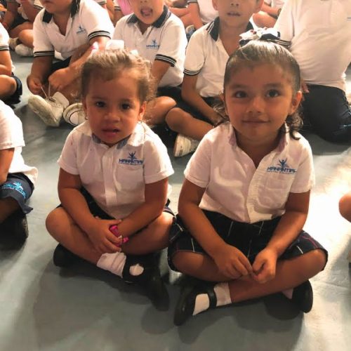 A group of children sitting on the floor in school uniforms.