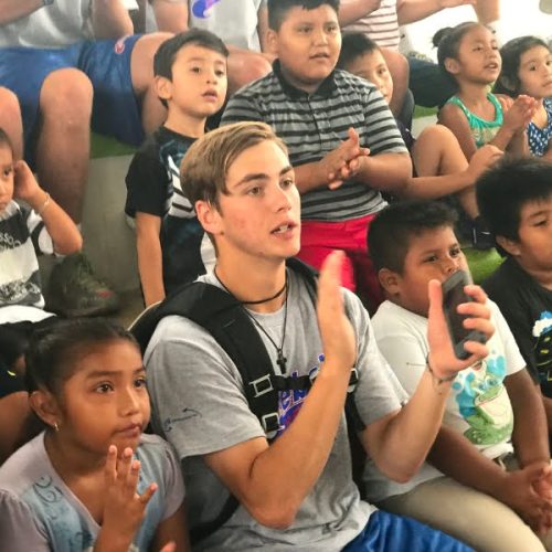 A man is sitting in front of a group of children.